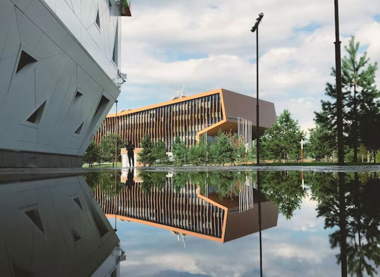 Modern buildings reflected in water, cloudy sky.